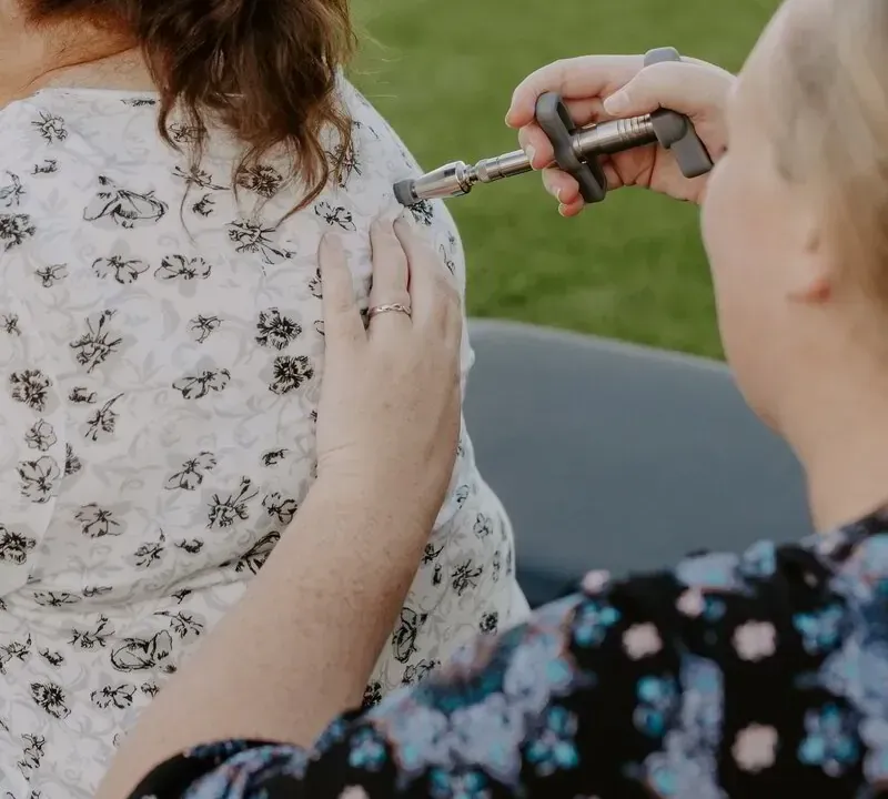 Dr. Caitlin Walker using a low-force adjusting instrument at the base of a patient's skull during migraine care in Oceanside